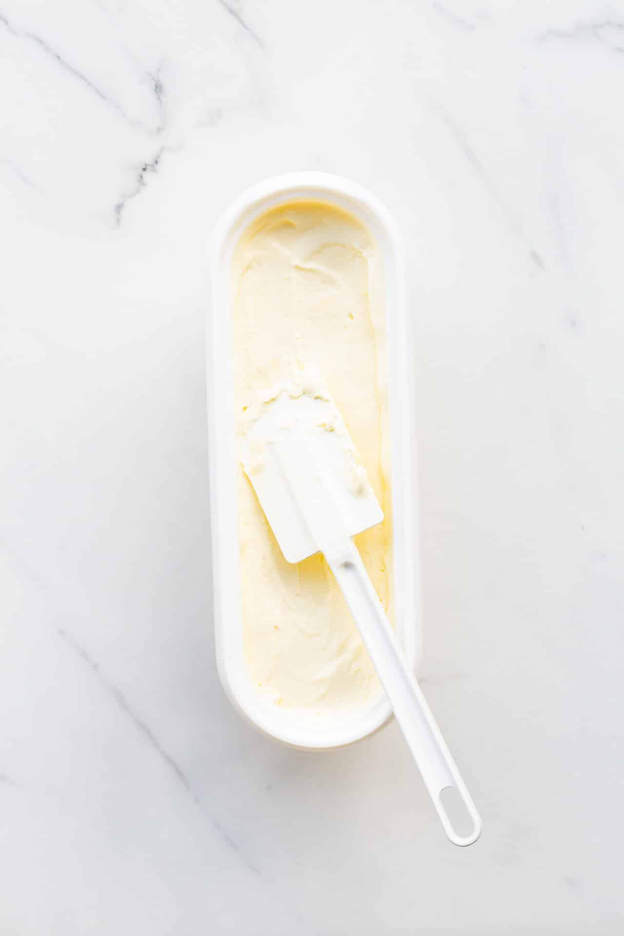 Freshly churned lemon ice cream transfered to a container with a white spatula before freezing