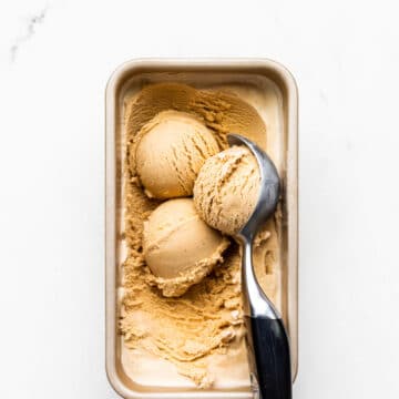 Scooping homemade black tea infused ice cream frozen in a loaf pan with a black handled ice cream scoop