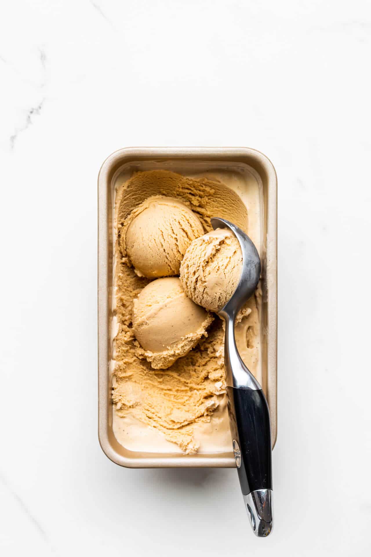 Scooping homemade black tea infused ice cream frozen in a loaf pan with a black handled ice cream scoop