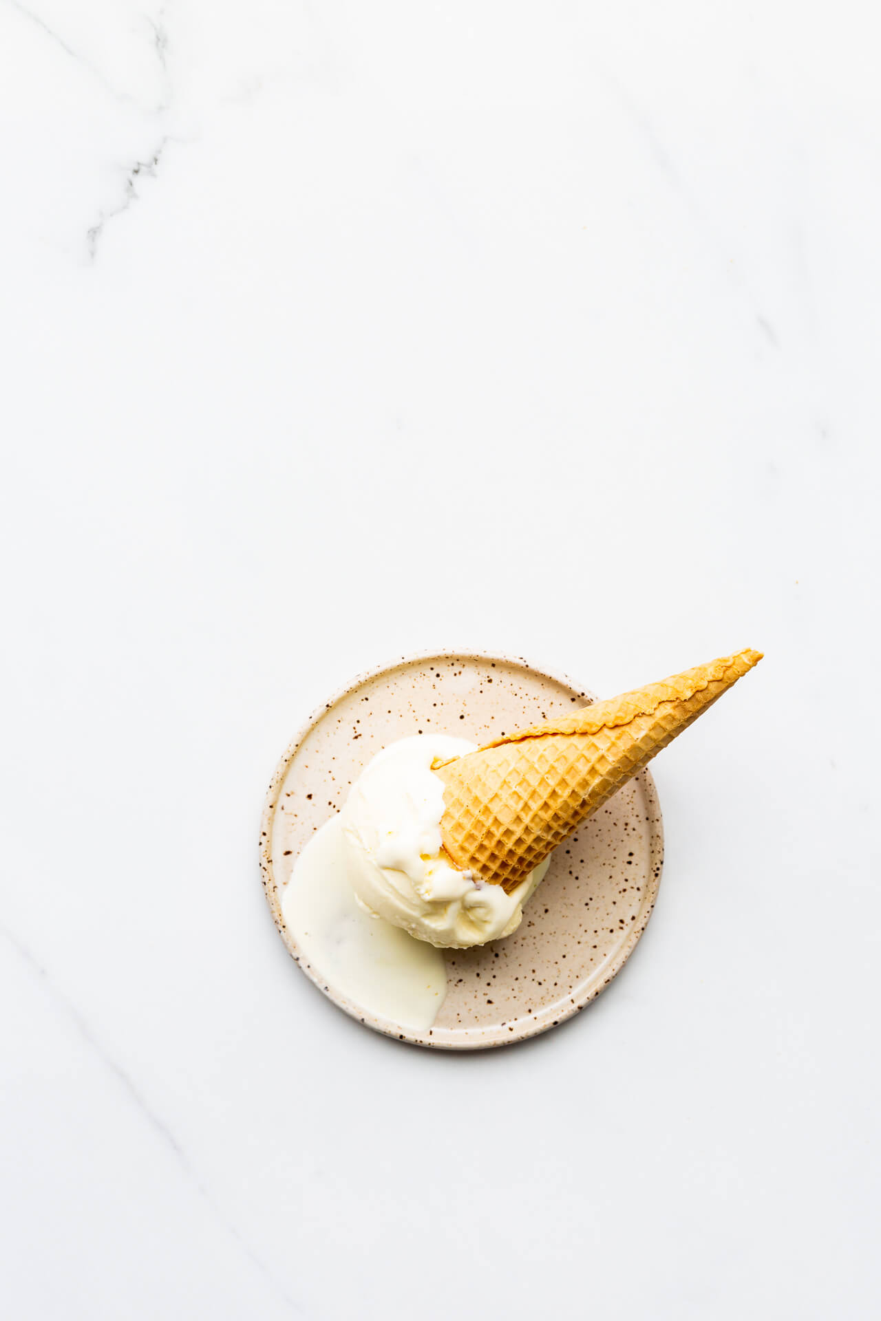 Lemon ice cream with cone on speckled plate, melting