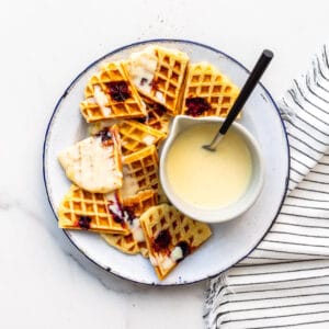 Cranberry waffles broken into pieces onto a plate and topped with crème anglaise to serve.