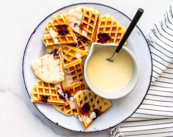Cranberry waffles broken into pieces onto a plate and topped with crème anglaise to serve.