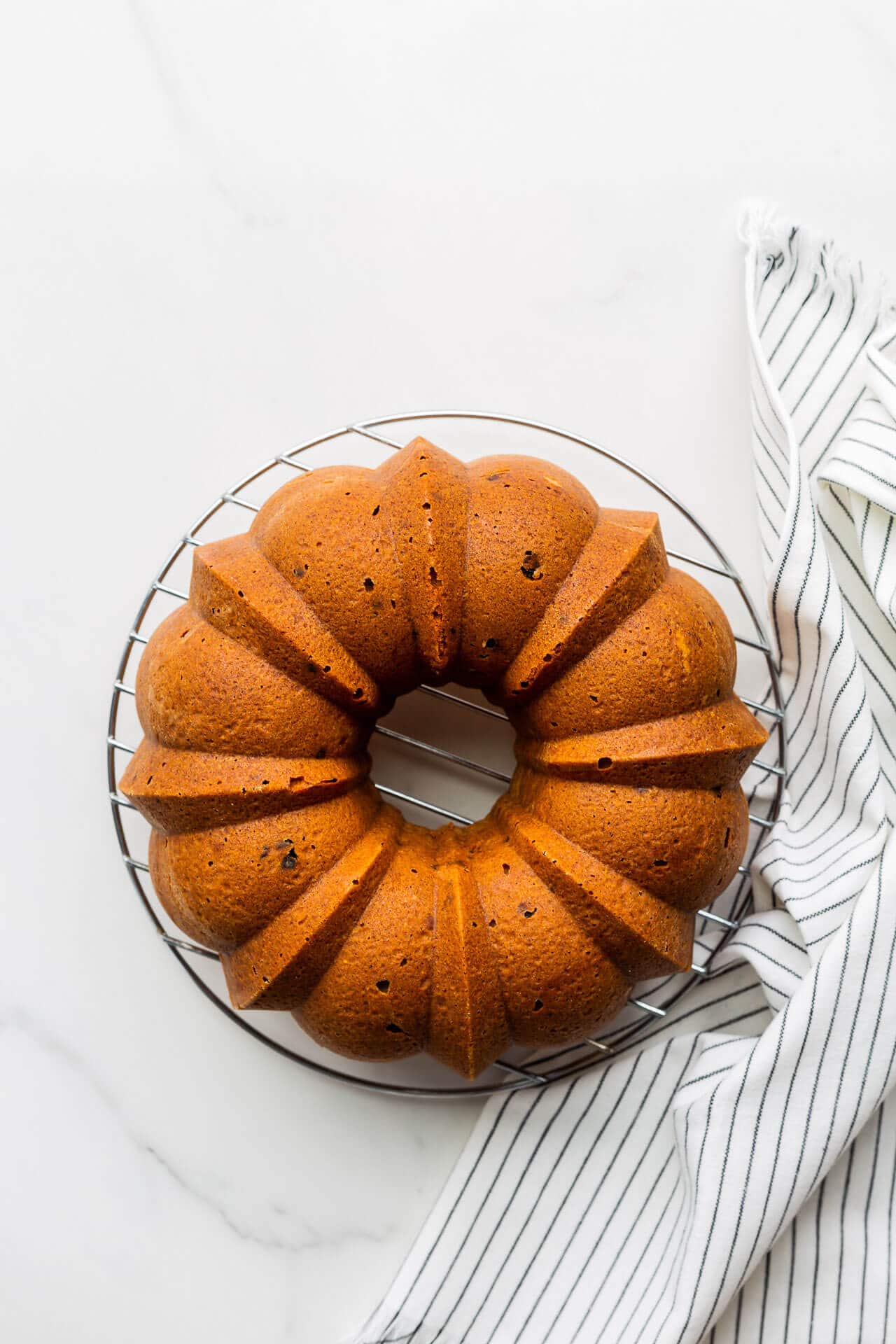 Bundt cake cooling on a round wire rack with striped linen nearby.