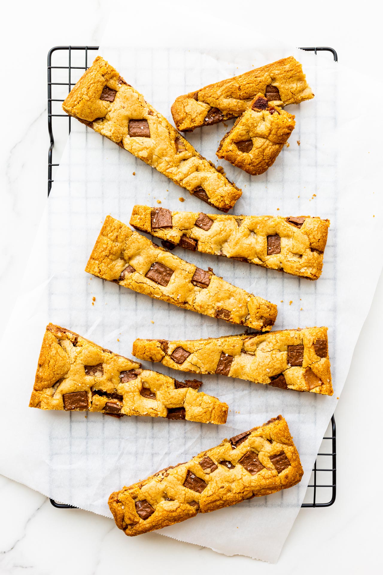 Chewy sea salt and toffee blondies cut into long bars on a black wire cooling rack.