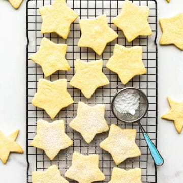 Star-shaped shortbread cookie on cooling rack with mini sifter of powdered sugar to sprinkle on top of the cookies