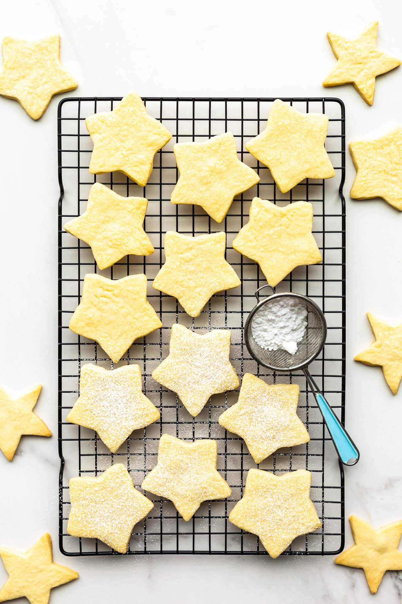 Star-shaped shortbread cookie on cooling rack with mini sifter of powdered sugar to sprinkle on top of the cookies.