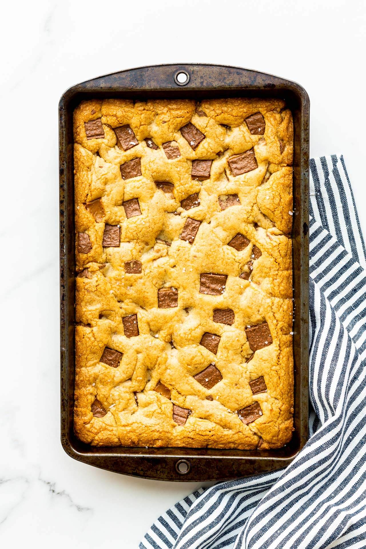 A rectangular pan of Skor blondie bars freshly baked with a striped towel