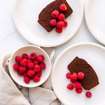 Slices of chocolate pound cake served on cream coloured plates with a bowl of fresh raspberries