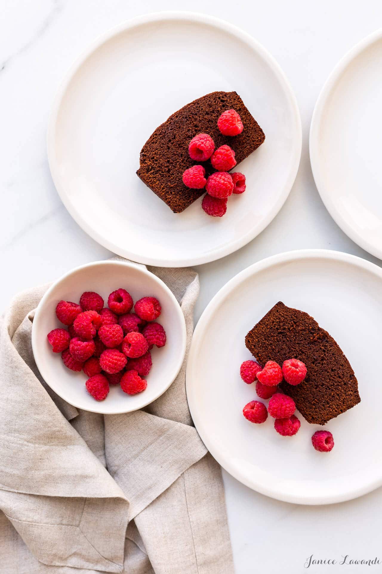 Slices of chocolate loaf cake served on cream coloured plates with a bowl of fresh raspberries