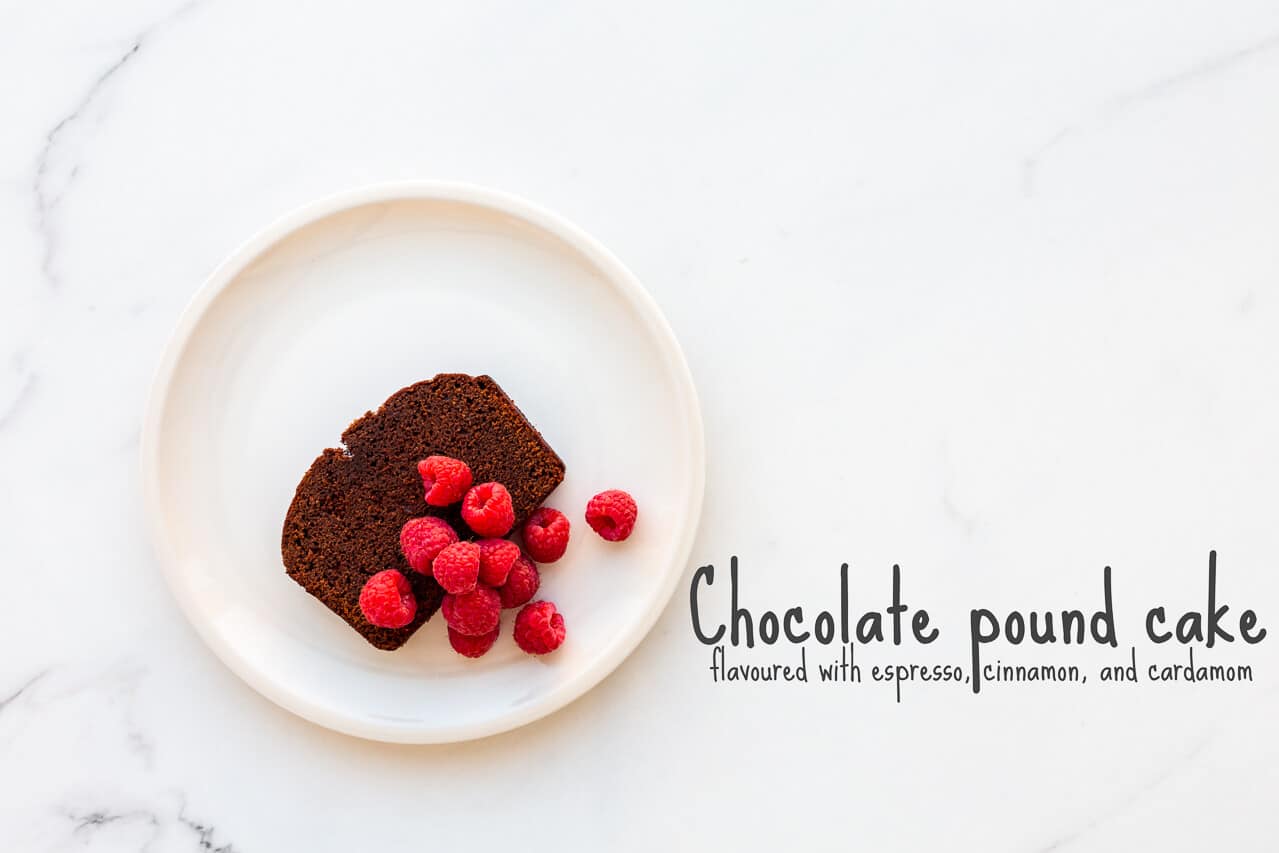 A slice of chocolate pound cake served on an off-white plate with fresh raspberries