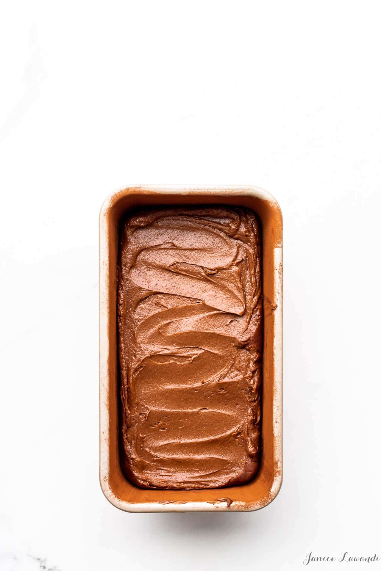 Chocolate cake batter swirled in a loaf cake pan that was prepared by buttering and dusting with cocoa powder to prevent the cake from sticking to the pan as it bakes