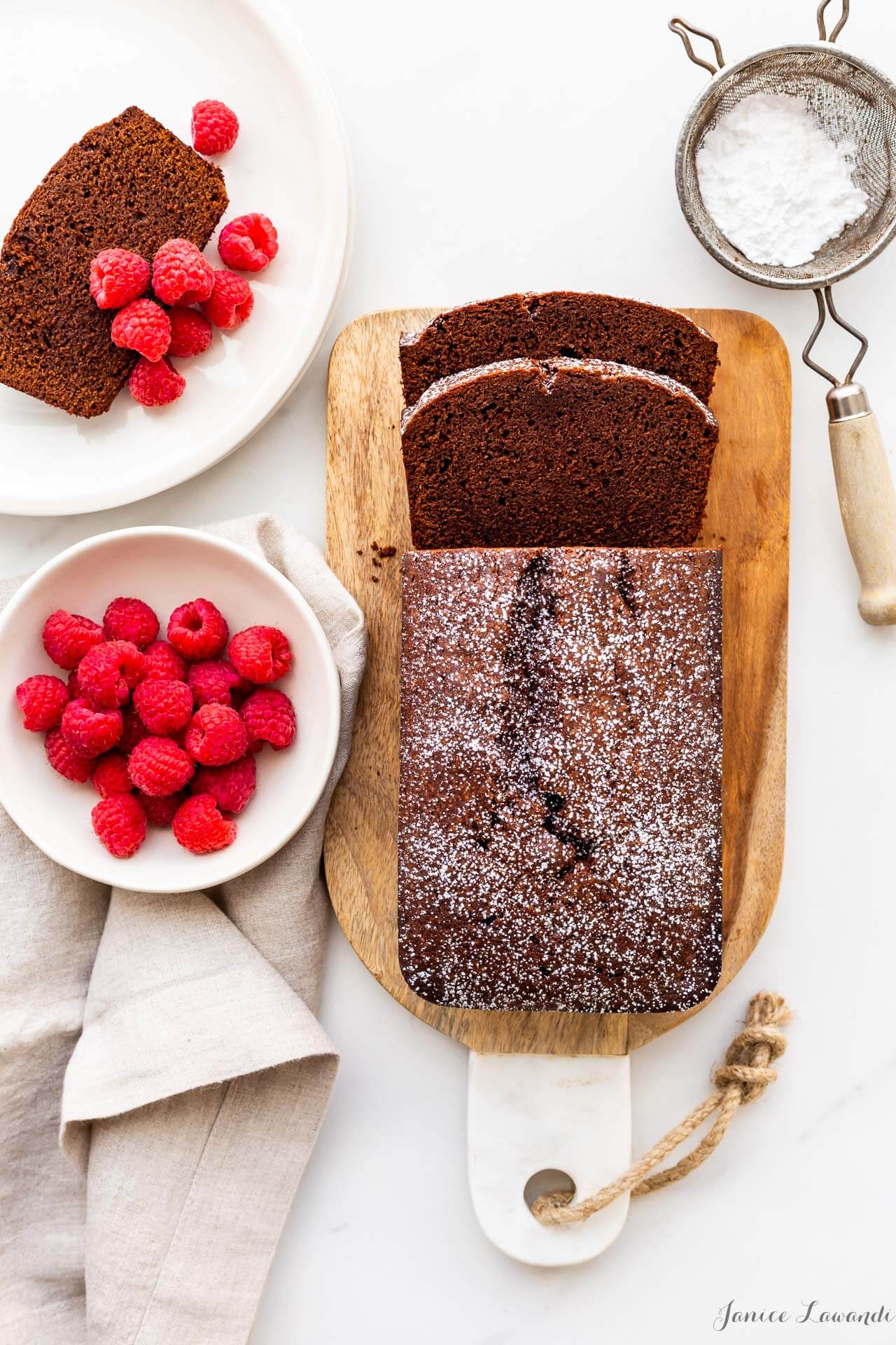 Slices of chocolate pound cake loaf cake flavoured with cinnamon and espresso, served on a cutting boards, slices topped with fresh raspberries