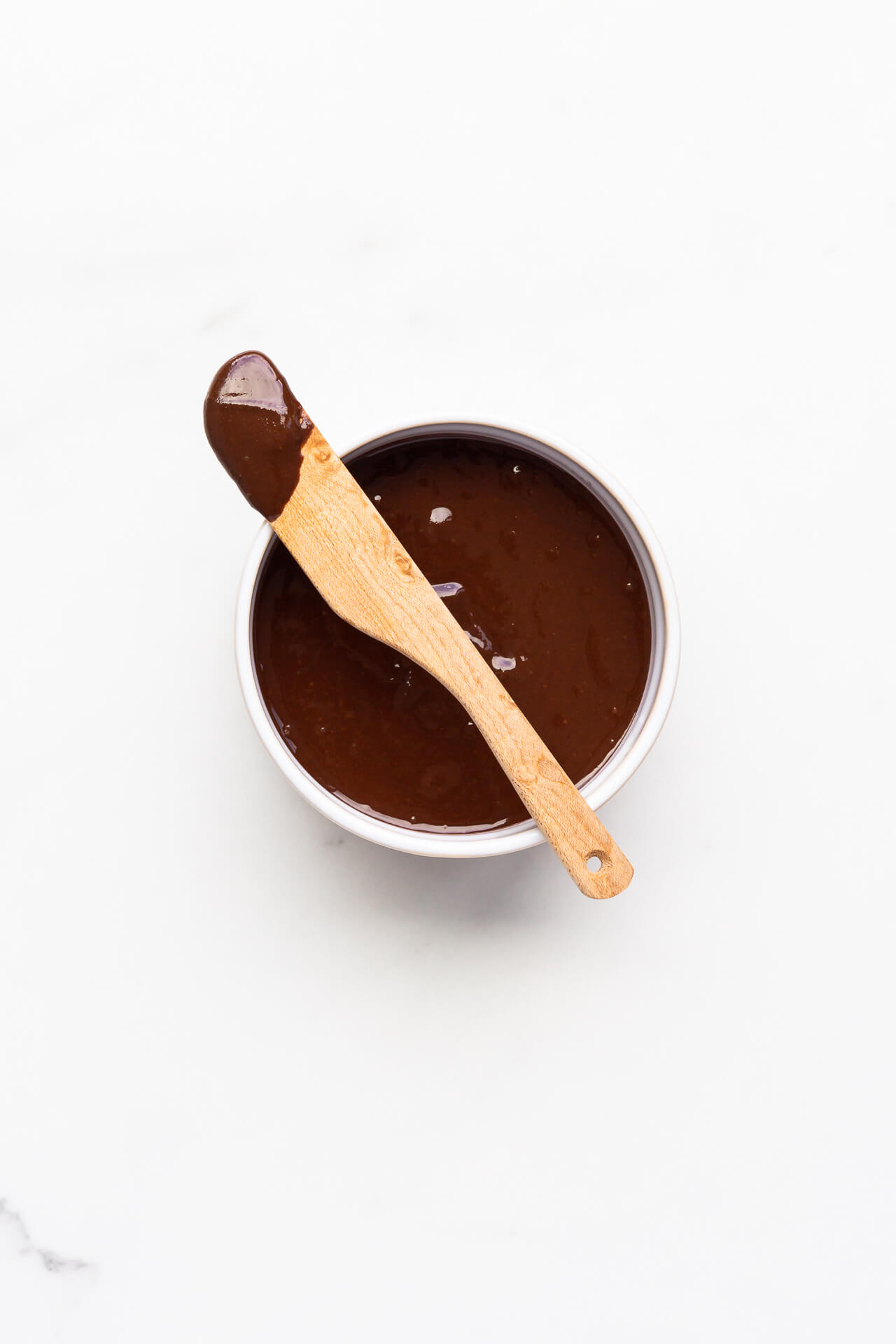 Chocolate tahini spread in a white bowl with a wooden spoon to serve it