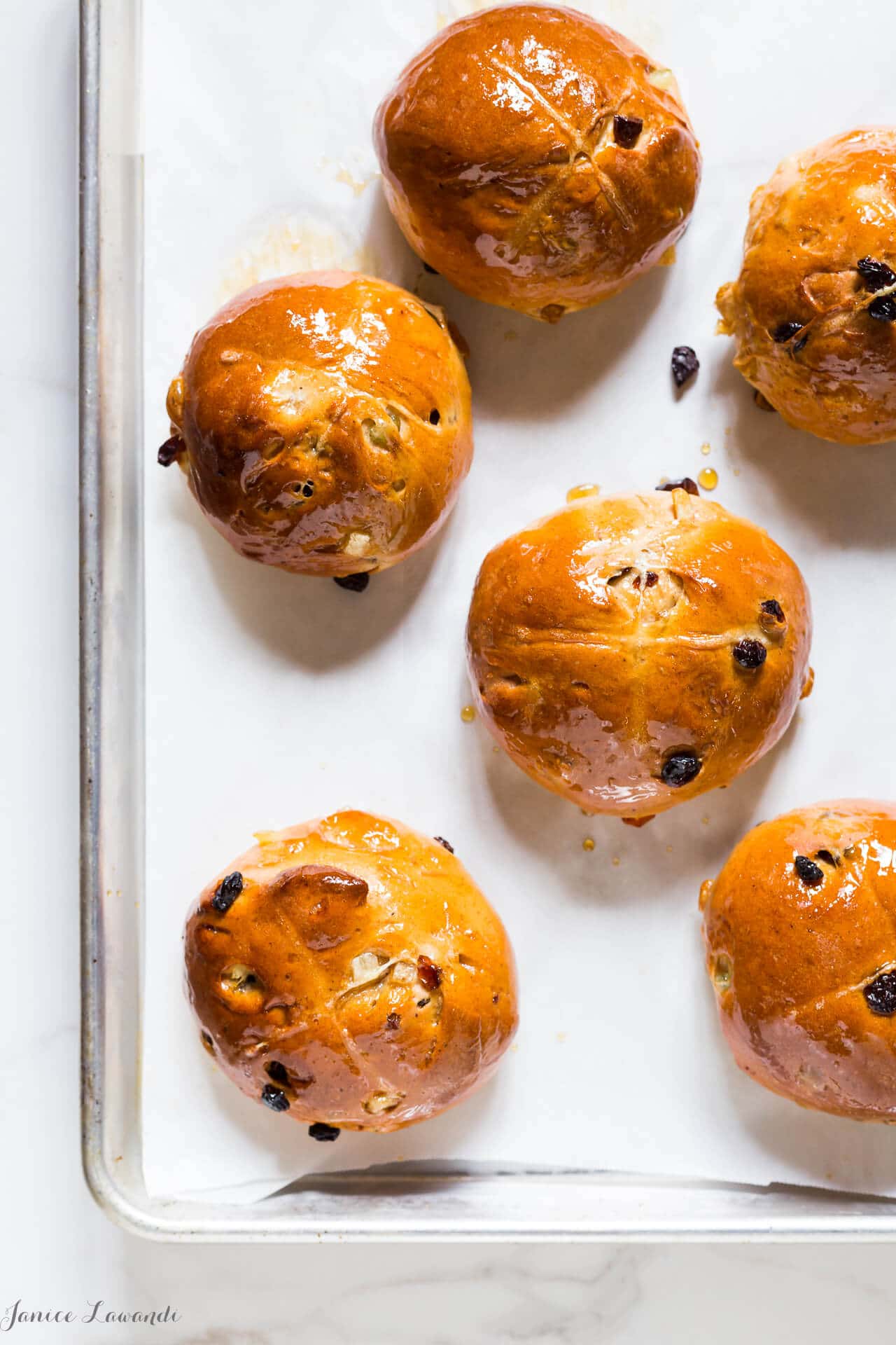 A baking sheet of round homemade hot cross buns with raisins and glazed with maple syrup