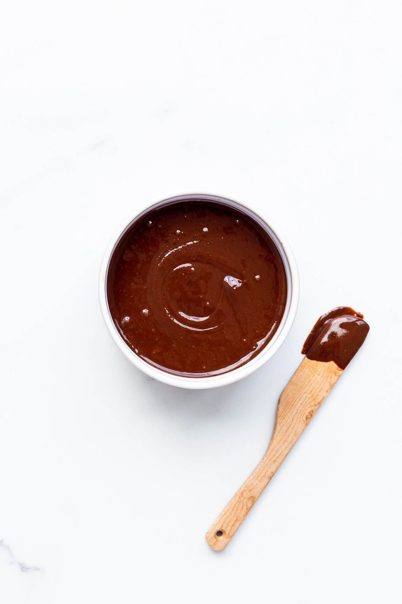 Chocolate tahini spread in a bowl with a wooden spoon dipped in it on the side.