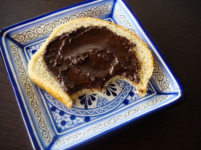 Homemade nutella on white bread with two bites taken out on a blue decorative square plate