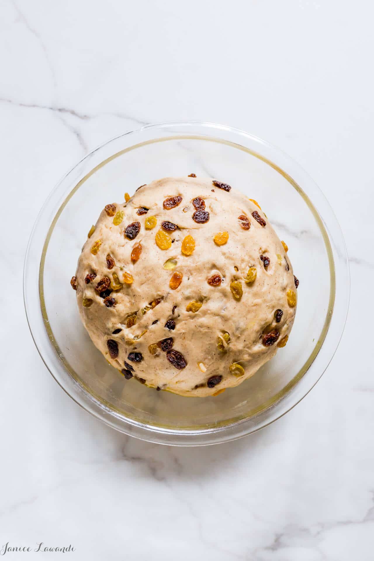 Hot cross bun dough with raisins before rising in a clear glass bowl