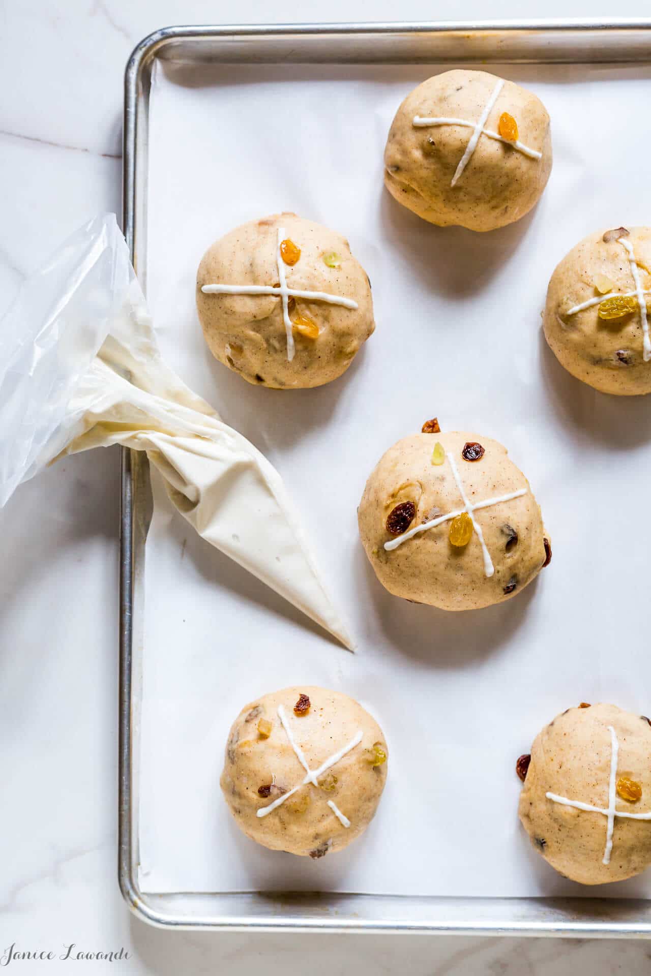 Piping flour paste onto hot cross buns with a piping bag after rising but before baking