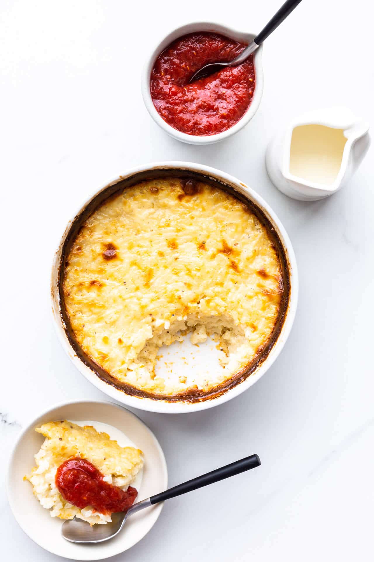 White ceramic dish of baked rice pudding served with rhubarb compote and cream on the side