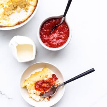 Baked rice pudding served in a small bowl with a drizzling of cream and a dollop of rhubarb compote