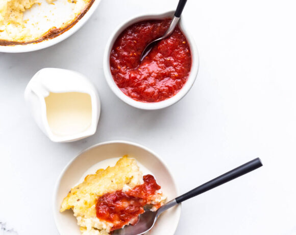 Baked rice pudding served in a small bowl with a drizzling of cream and a dollop of rhubarb compote