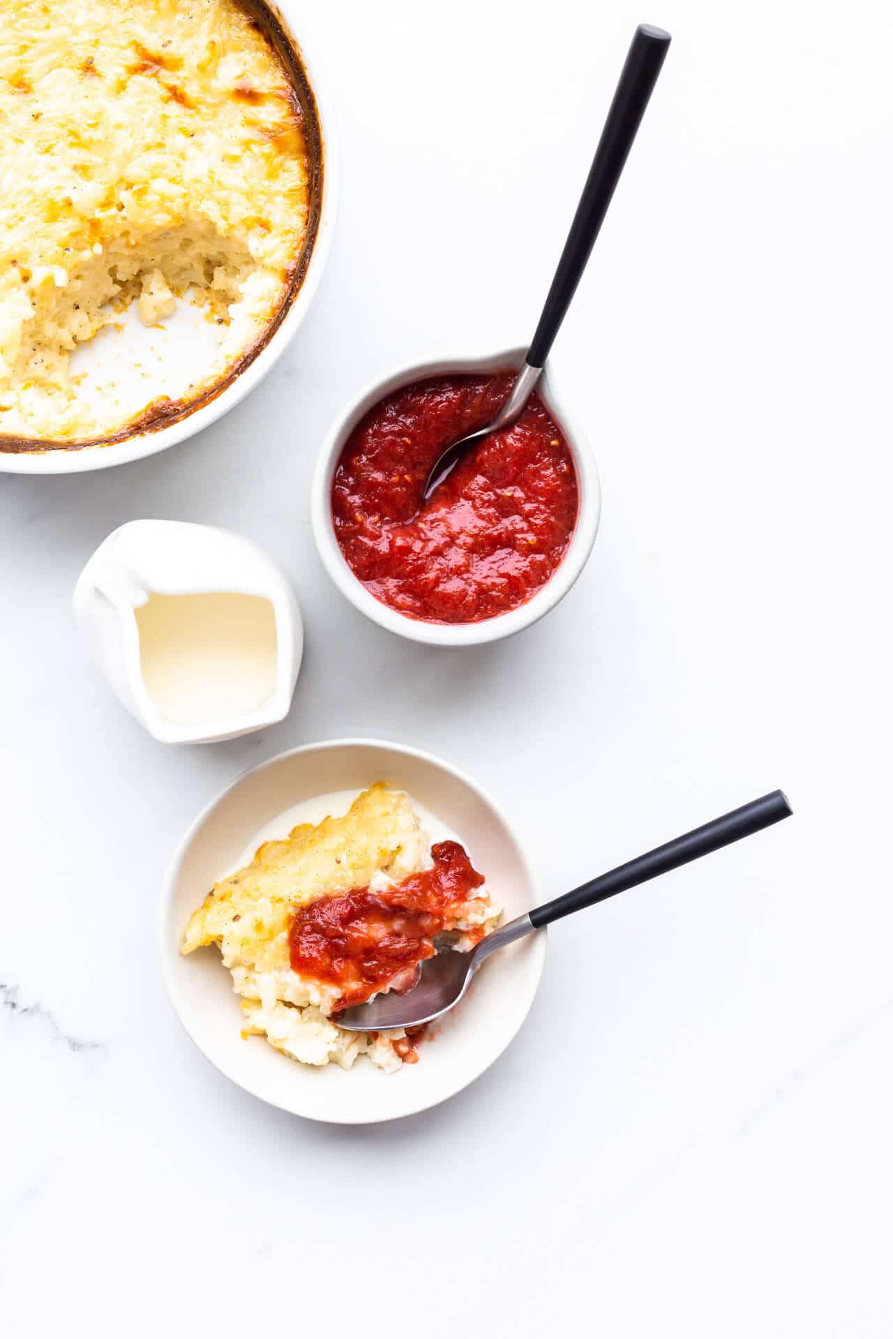 Baked rice pudding served in a small bowl with a drizzling of cream and a dollop of rhubarb compote