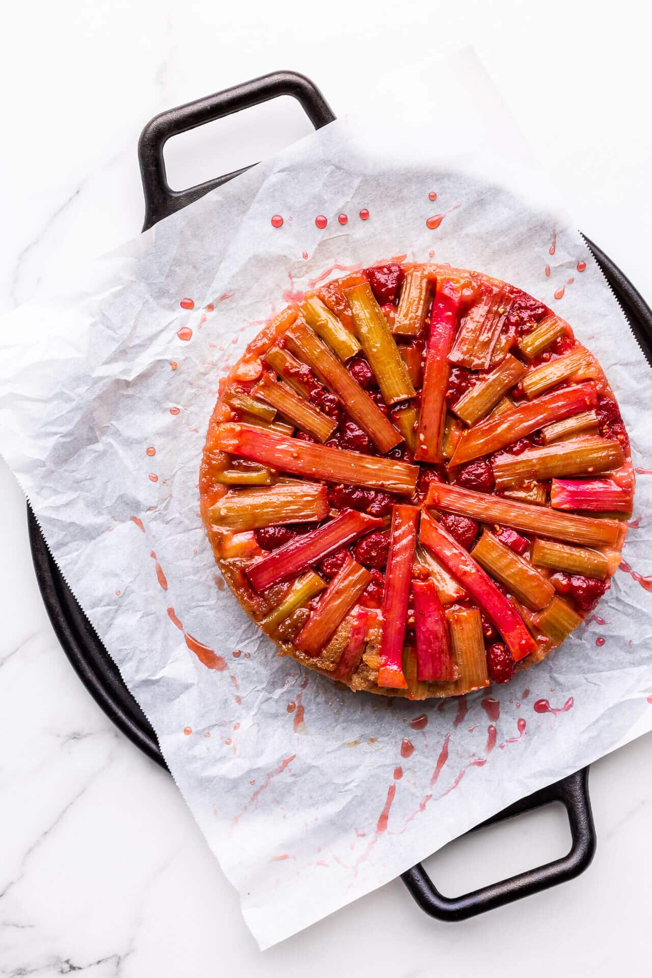 Raspberry rhubarb upside down cake on a parchment lined black round tray