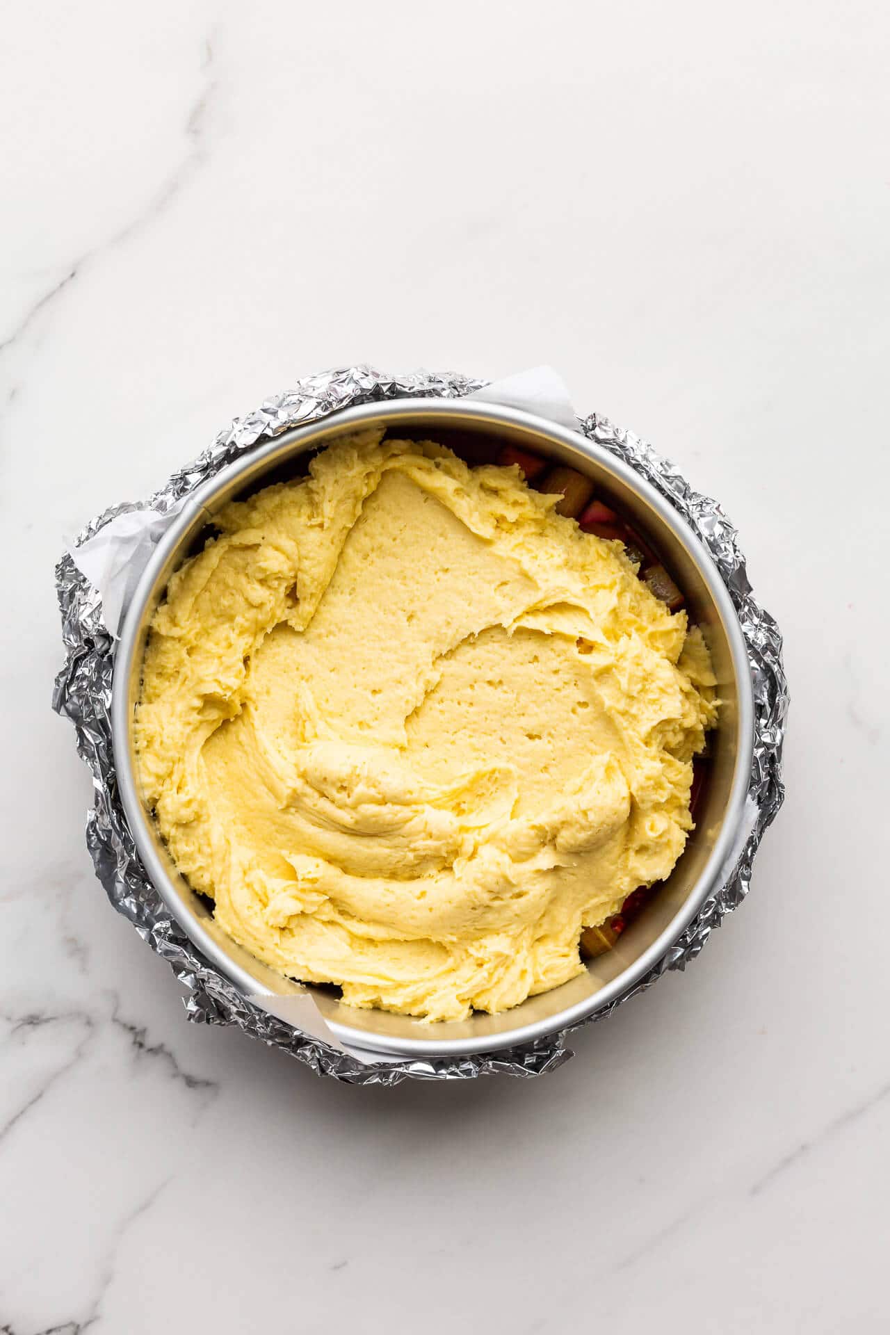 Spreading cake batter over a fruit and caramel layer to make an upside down cake in a springform pan wrapped in foil to stop the juices from leaking out