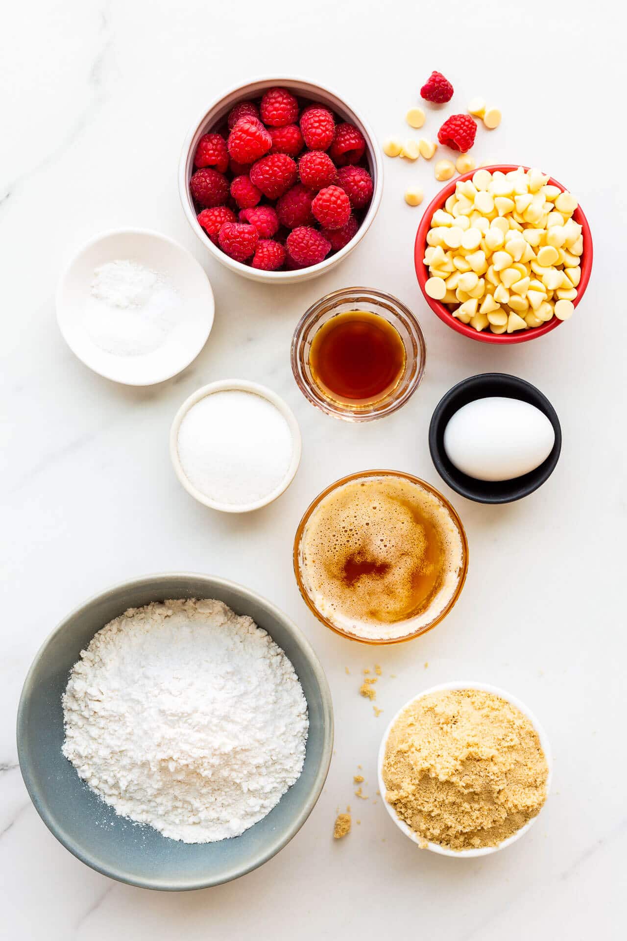 Ingredients measured out to make blondies with fresh raspberries and white chocolate, as well as flour, brown sugar, white sugar, browned butter, salt, baking powder, baking soda,1 egg, vanilla extract.