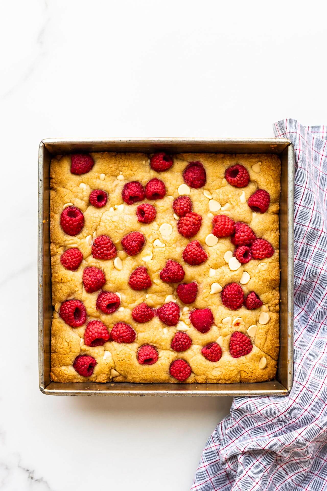 An 8x8 inch pan of baked blondies with raspberries and white chocolate chips on top