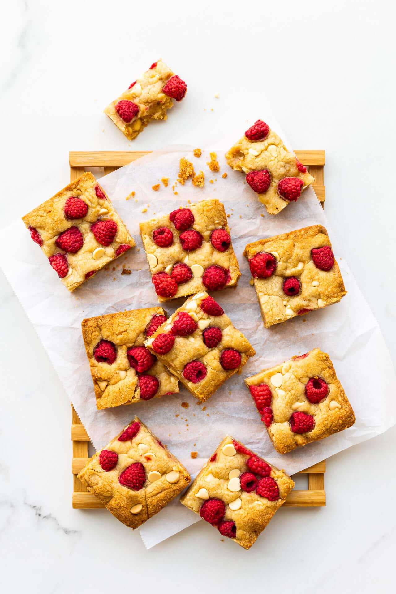 White chocolate and raspberry blondies cut into squares on a parchment-lined wood serving board