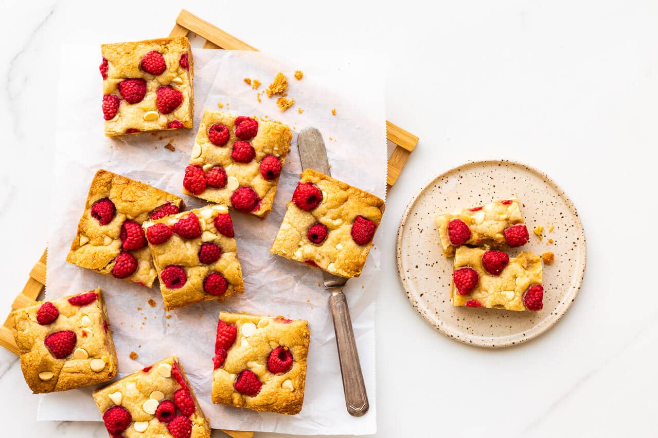 Squares of raspberry white chocolate blondie bars served with a knife on a speckled ceramic plate