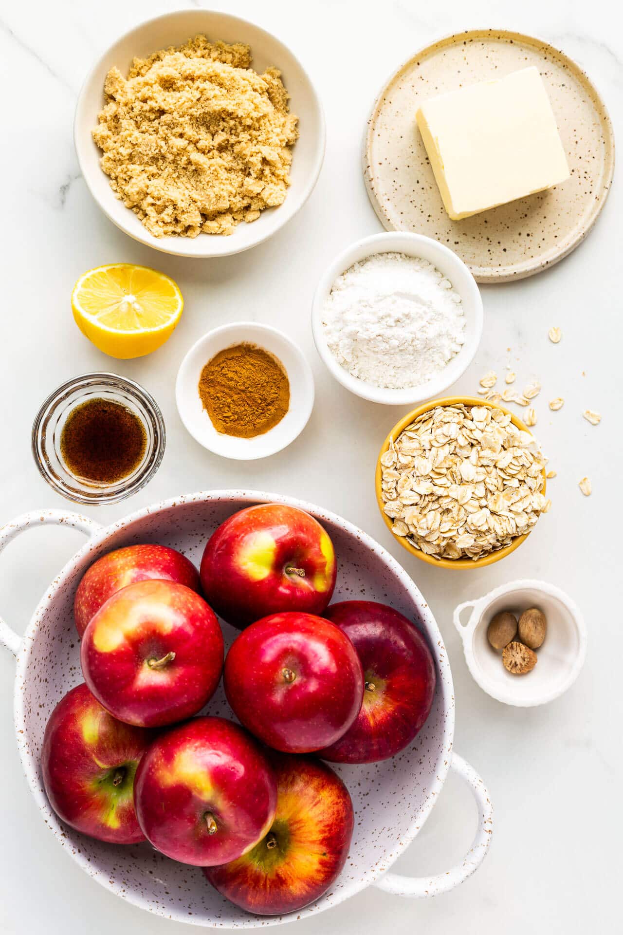 Ingredients to make apple crisp measured out including apples, brown sugar, butter, flour, oats, cinnamon, nutmeg, vanilla bean paste, and a little lemon juice for the apples