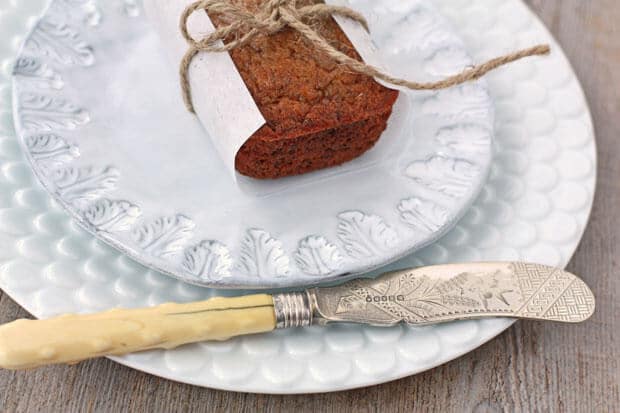 Mini Banana bread loaf wrapped in parchment and tied with string on light blue ceramic plate layered on white scalloped plate