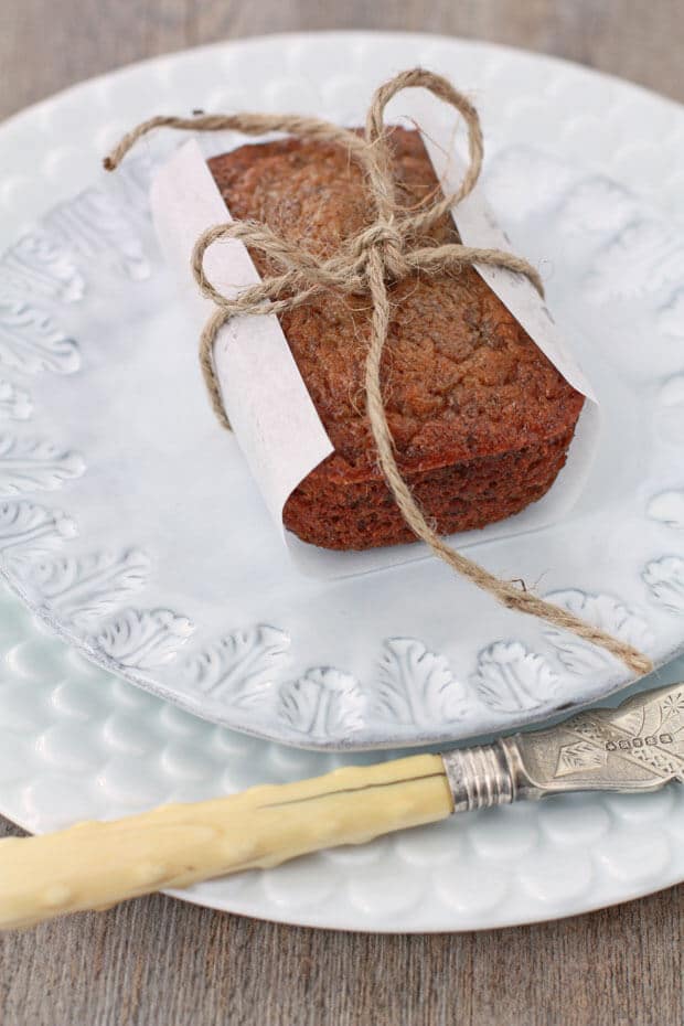 Mini banana bread loaf wrapped in parchment and tied with kitchen twine on a light blue ceramic plate