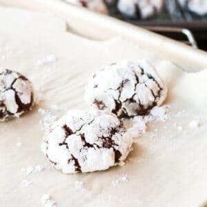 Chocolate crinkle cookies coated in icing sugar on a parchment-lined sheet pan.