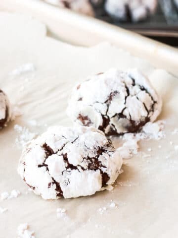 Chocolate crinkle cookies coated in icing sugar on a parchment-lined sheet pan.