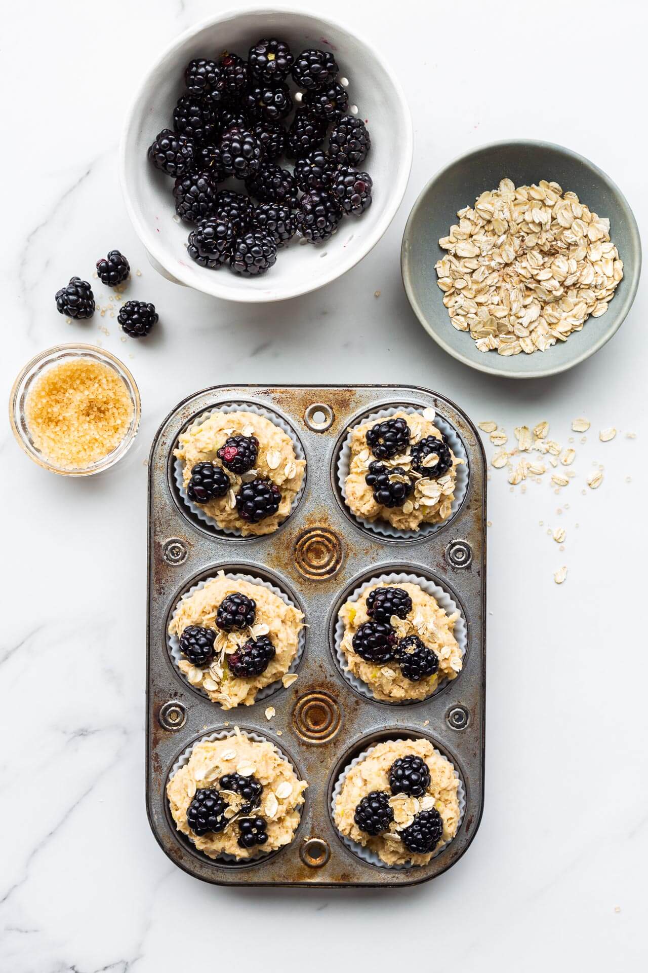 Finishing apple blackberry muffins placing blackberries, oats, and turbinado sugar on top before baking