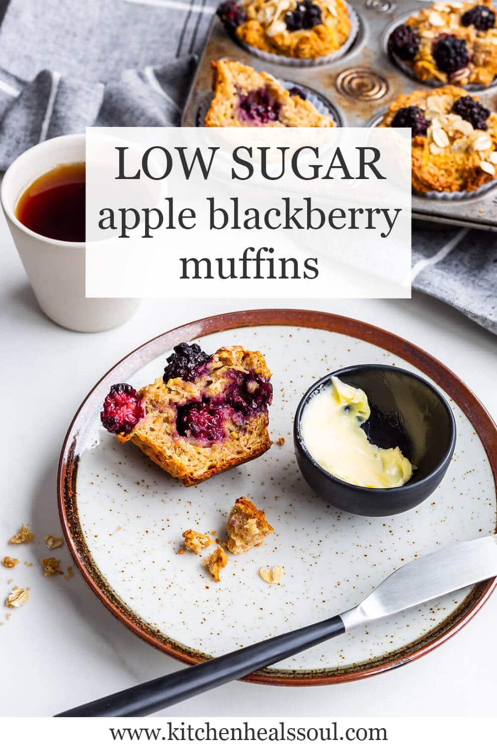 Low sugar apple blackberry muffins with a vintage muffin pan of baked muffins in the background, a cup of black tea, and a speckled ceramic plate with half a muffin and a dish of butter + knife