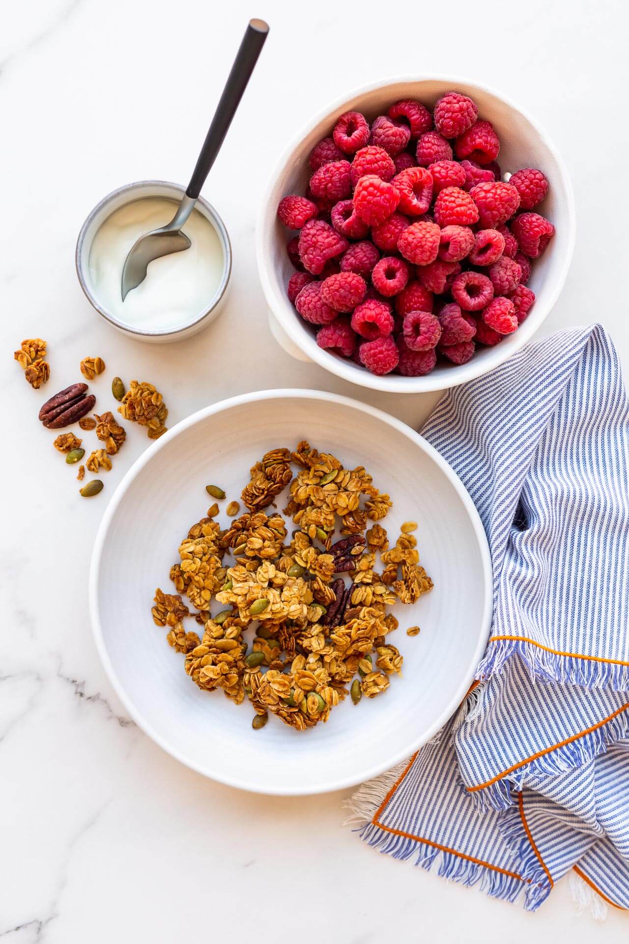 A bowl of granola clusters served with a bowl of berries and greek yogurt, striped linen napkin