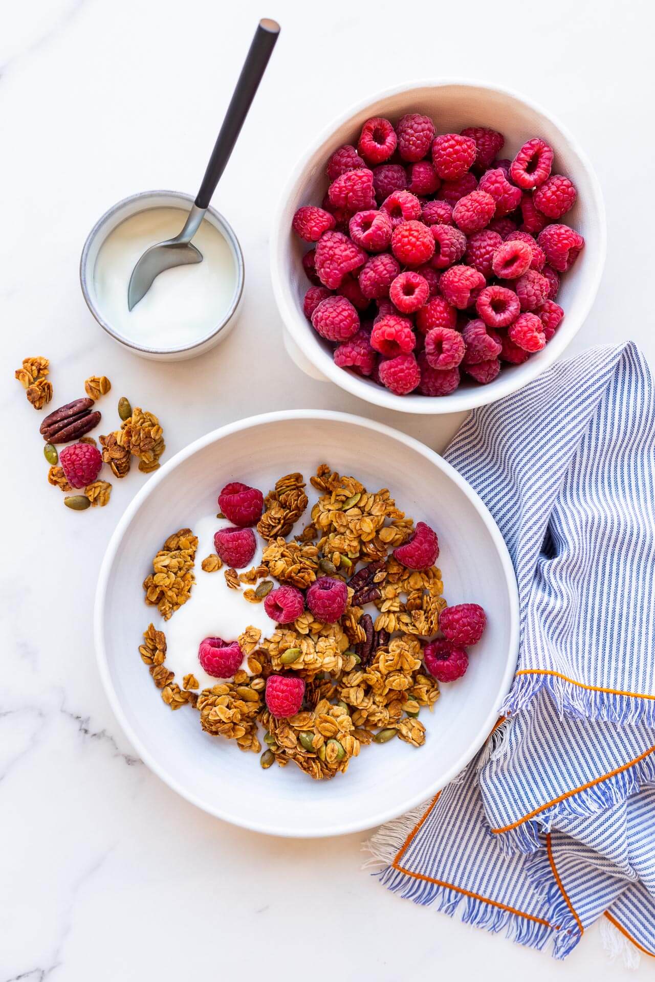Bowl of granola clusters with yogurt and raspberries, striped linen napkin