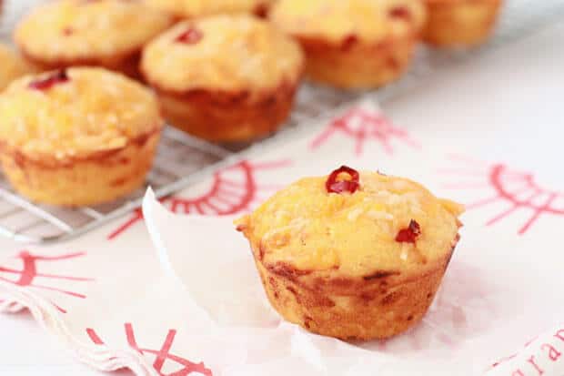 Chili cheddar cornbread muffins cooling on a cooling rack with one set on a square of parchment on red and white napkin.