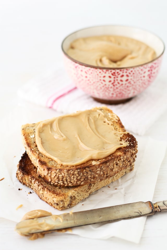 Homemade maple butter on toast smeared with a knife from a red and white bowl of maple butter
