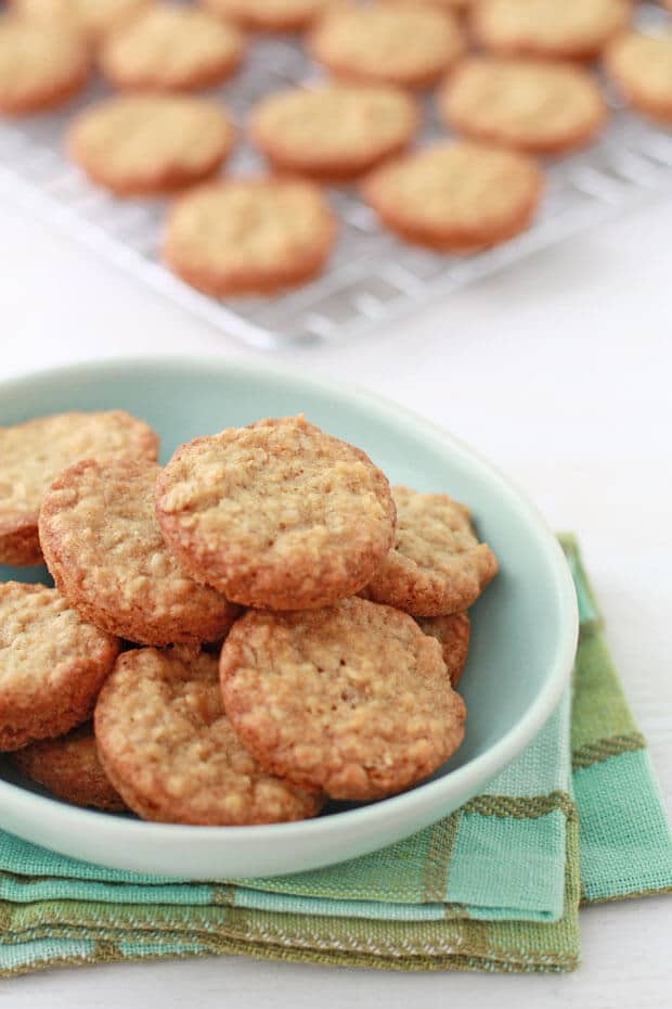 Mini thick oatmeal cookies in a turquoise bowl with more cookies cooling on a wire rack behind.