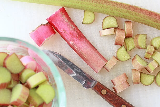 Chopping and slicing fresh rhubarb with a small pairing knife on a white cutting board