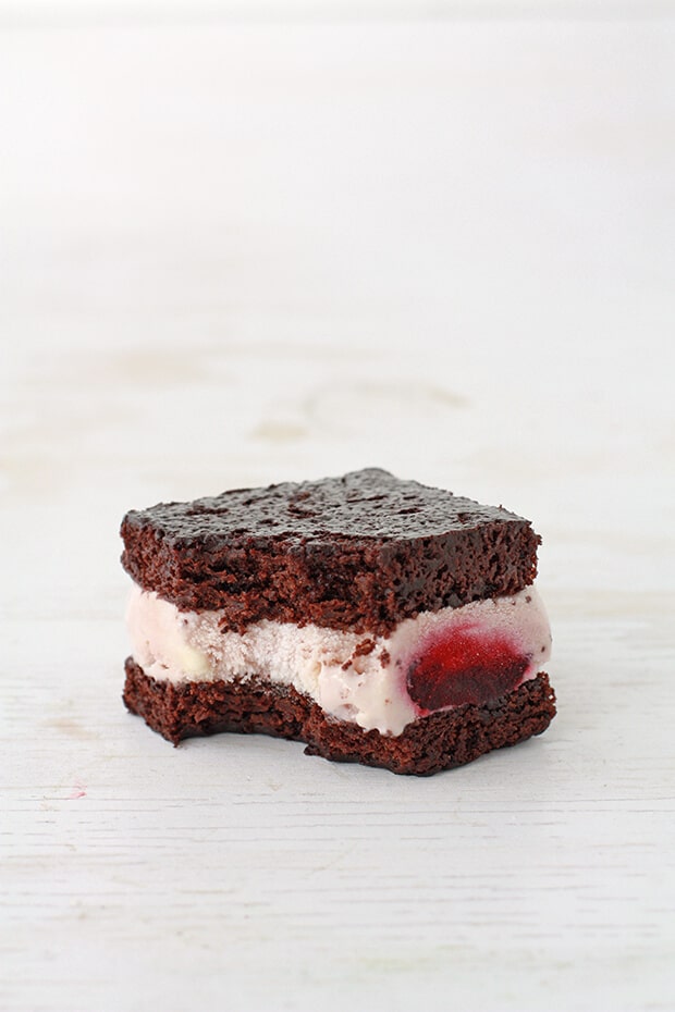 Homemade ice cream sandwich with cherry ice cream and brownie cake, with a bite taken out to show inside.