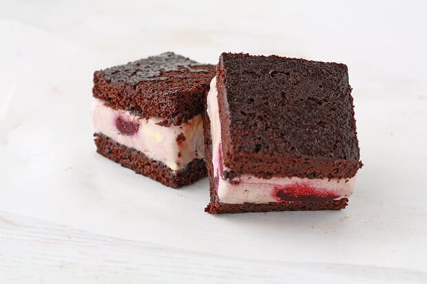 Two homemade ice cream sandwiches made with chocolate cake and cherry ice cream so you can see whole cherries in the ice cream layers.