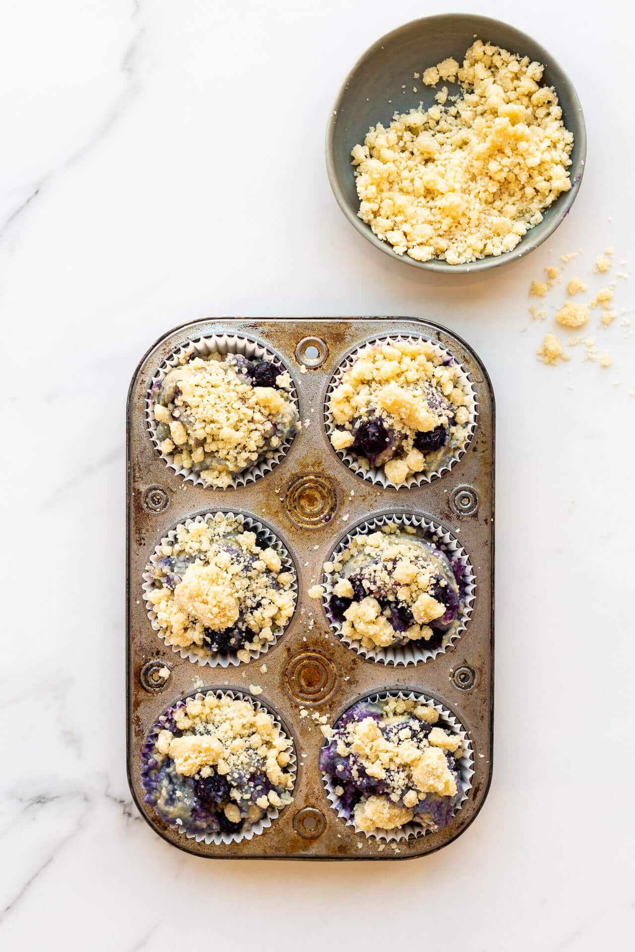 Topping blueberry muffins with streusel topping in a vintage muffin pan before baking