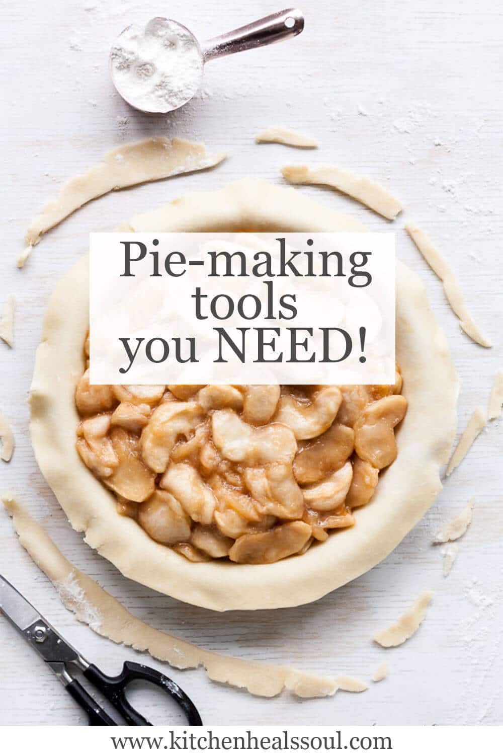 Apple pie being made with bottom crust in pan, topped with apple pie filling, scissors for trimming excess crust around edges and a little cup of flour for dusting if more pastry rolling is needed