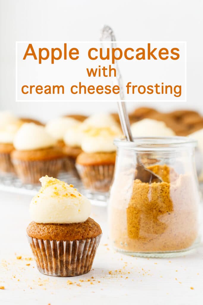 Mini apple cupcakes topped with dollops of cream cheese frosting and sprinkled with spoonfuls of graham cracker crumbs from a jar.